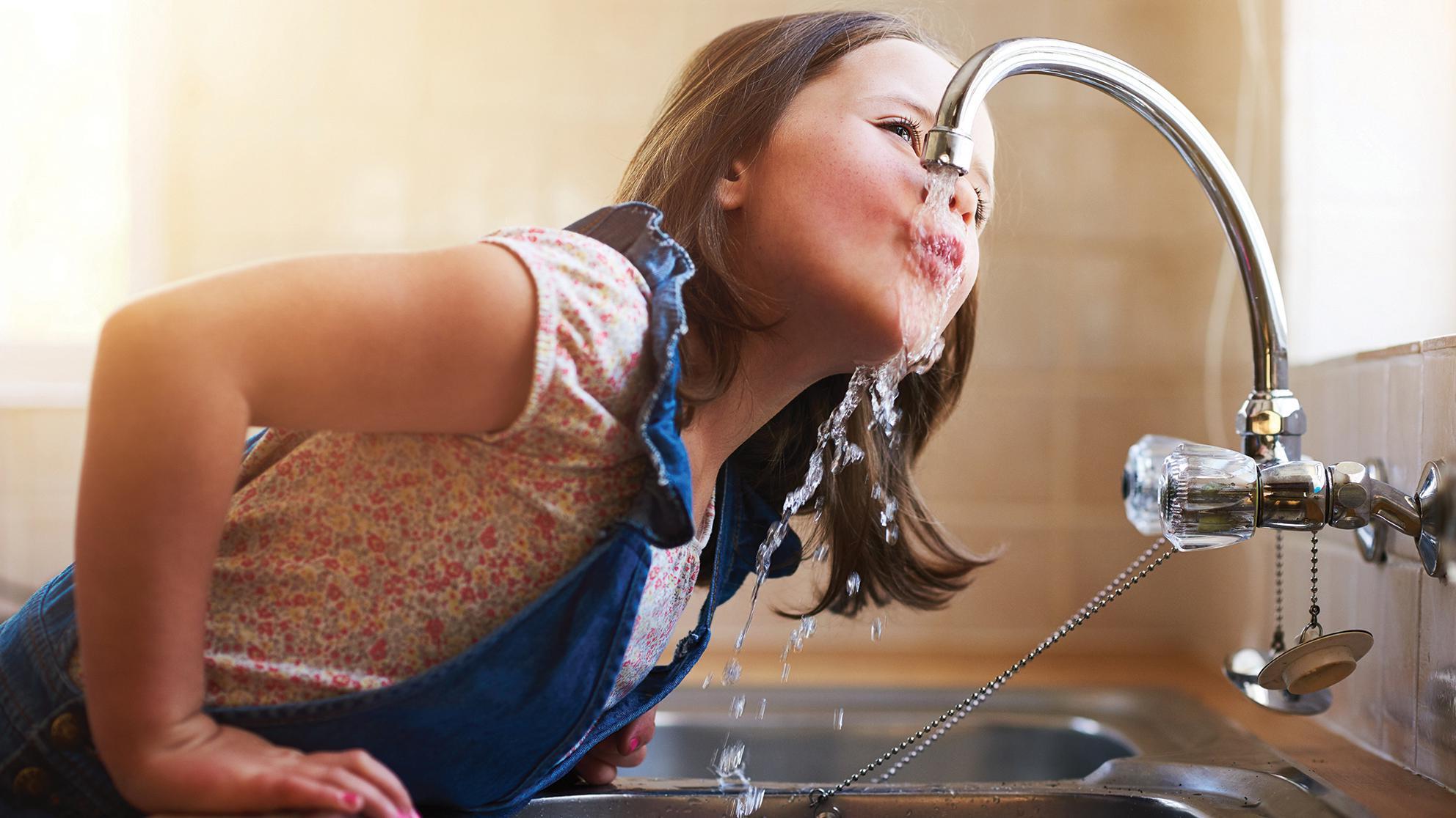 Child drinking water from kitchen sink faucet 